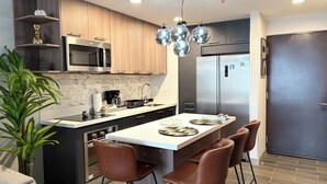 A modern kitchen with a central island, stainless steel appliances, and a dining area with brown leather chairs. - Cozy Apartment 10 min to Airport Be Cariari Condo new (Ulloa)