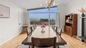 Une salle à manger avec une grande table en bois, des chaises, un lustre, une bibliothèque et une vue sur l’extérieur.