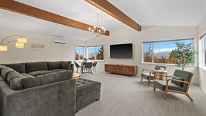 Un salon moderne comprenant un canapé d’angle, un meuble en bois, un coin repas et de grandes fenêtres offrant une vue dégagée.