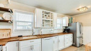 A kitchen with white cabinets, a wooden countertop, a stainless steel refrigerator, and a window with blinds. - The Prettiest Palm |Kayak, Beach Toys & Cornhole | 3mins to Beach | Community Pool | Fenced Yard (Jamaica Beach)