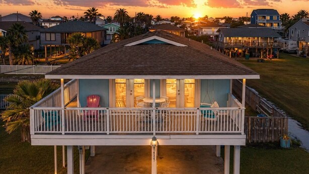 A house with a covered porch, a pool, and a view of the neighborhood. - The Prettiest Palm |Kayak, Beach Toys & Cornhole | 3mins to Beach | Community Pool | Fenced Yard (Jamaica Beach)
