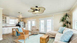A spacious living room with a beige sofa, a wicker chair, a wooden coffee table, and a ceiling fan. - The Prettiest Palm |Kayak, Beach Toys & Cornhole | 3mins to Beach | Community Pool | Fenced Yard (Jamaica Beach)