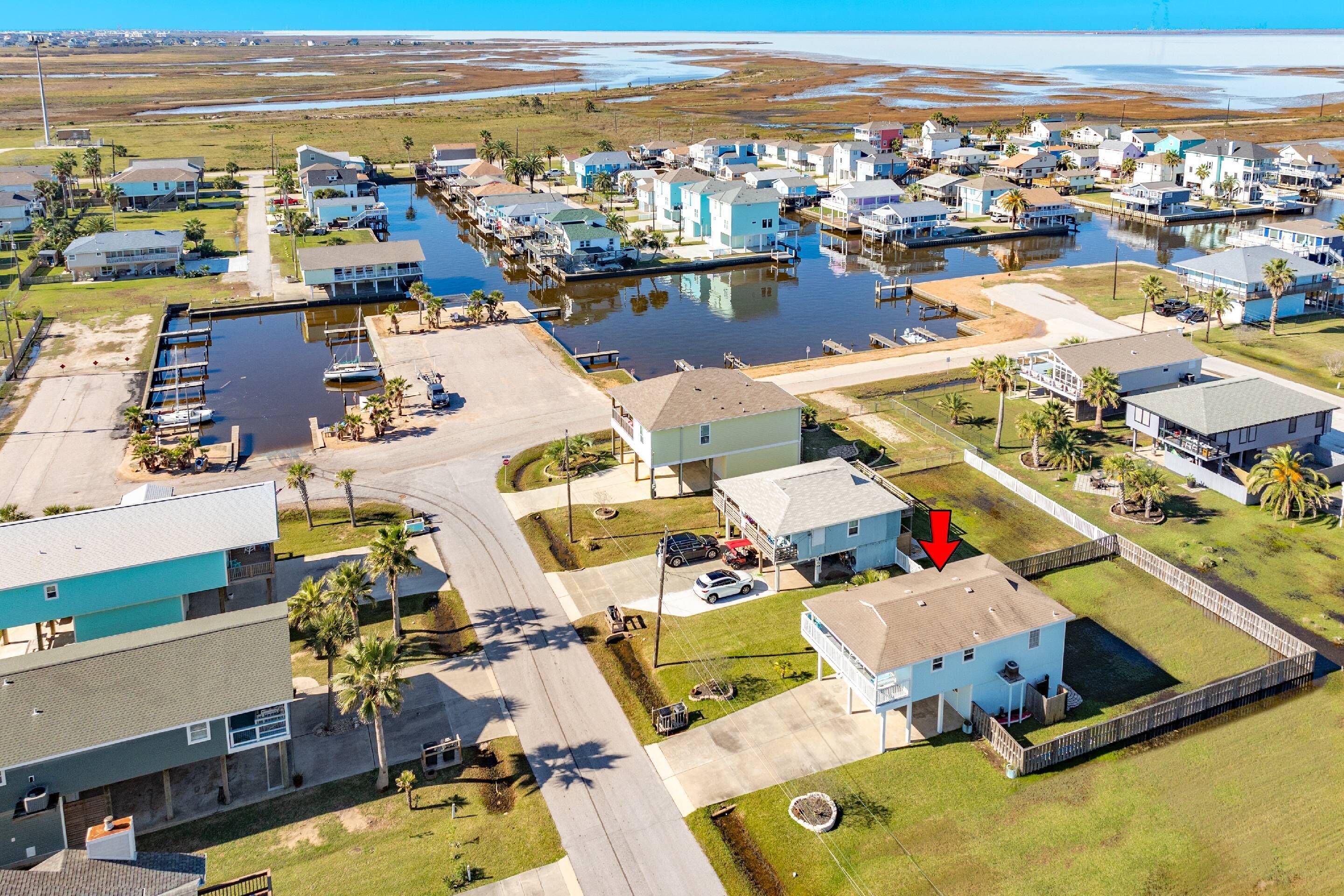 An aerial view of a coastal residential area with houses, a marina, and a road.