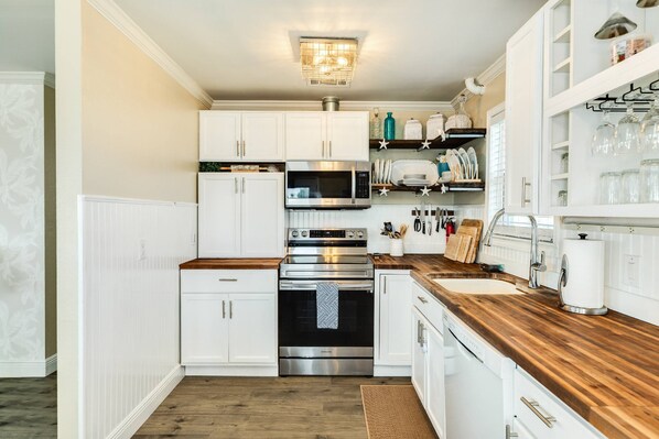 Cocina moderna con armarios blancos, electrodomésticos de acero inoxidable y encimera de madera.