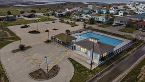 An aerial view of a residential area with a swimming pool, a parking lot, and houses. - The Prettiest Palm |Kayak, Beach Toys & Cornhole | 3mins to Beach | Community Pool | Fenced Yard (Jamaica Beach)