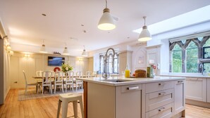 A modern kitchen with a central island, wooden flooring, white cabinetry, and pendant lighting. - Oakland West - Windermere, Sleeps 14 (Windermere)
