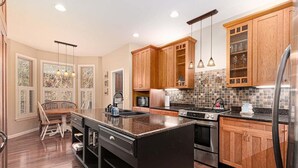 Una cocina moderna con armarios de madera, una isla grande, electrodomésticos de acero inoxidable y un comedor con mesa y sillas de madera.