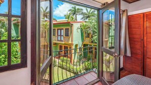 A room with a sliding glass door leading to a balcony with a view of a green building and palm trees. - Hidden Paradise LS17 -Minutes to All the Action! (Tamarindo)