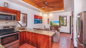 A kitchen with wooden cabinets, a granite countertop, a built-in oven, a microwave, and a refrigerator. - Hidden Paradise LS17 -Minutes to All the Action! (Tamarindo)