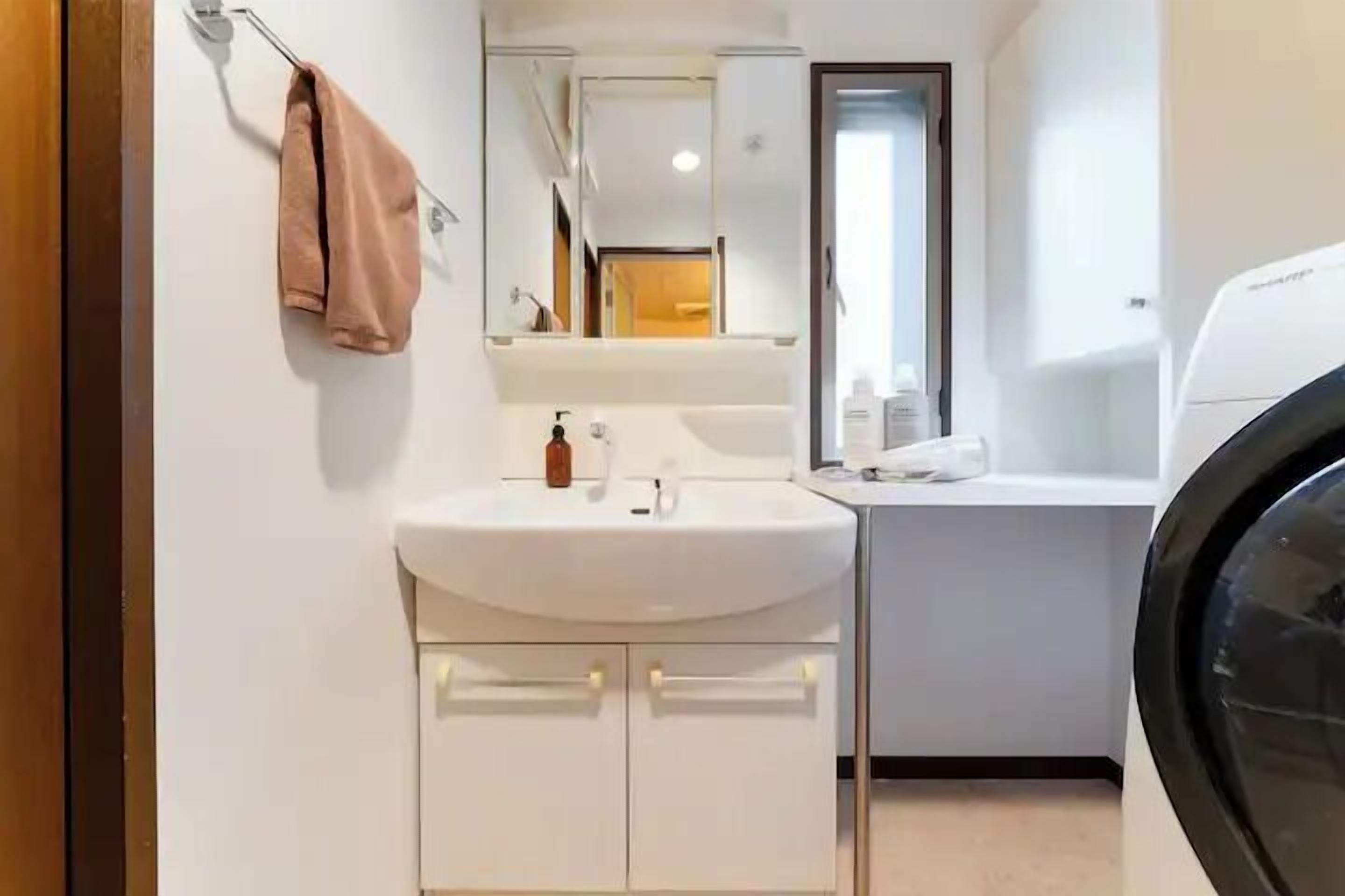 A modern bathroom with a white sink, mirror, and a black washing machine.