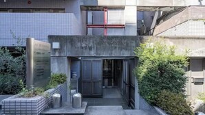 Un edificio moderno con facciata in cemento, un cartello metallico e un piccolo ingresso con gradini.