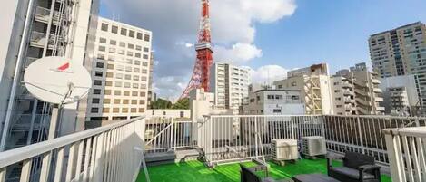 A rooftop terrace with a green carpet, outdoor furniture, and a view of the Tokyo Tower.
