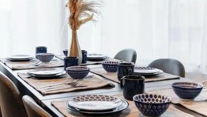 Un tavolo da pranzo apparecchiato con piatti, ciotole e un vaso con fiori secchi.