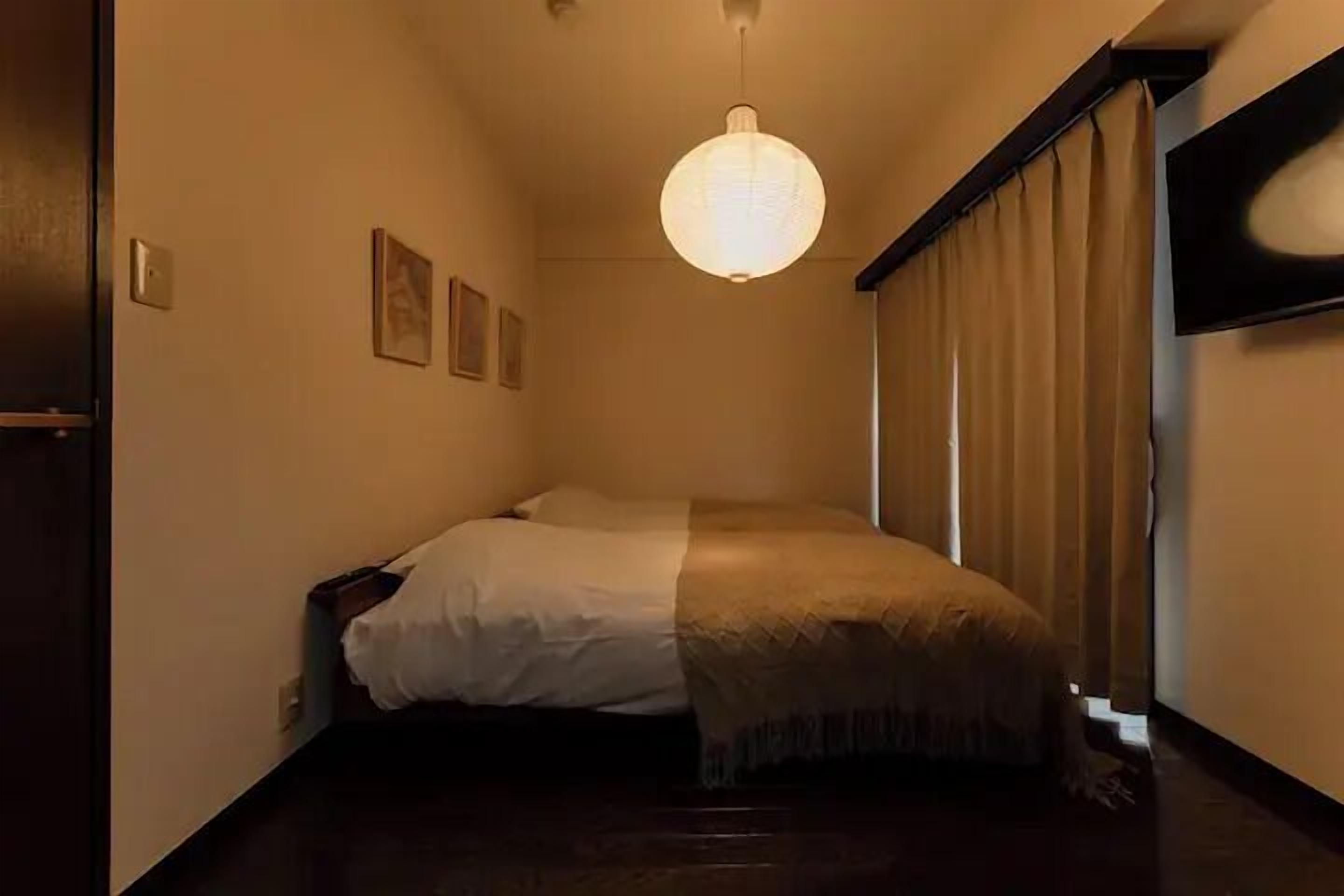 A bedroom with a bed, a hanging light fixture, and a window with curtains.