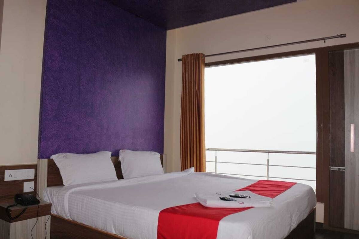 Ein Hotelzimmer mit einem großen Bett, einem Fenster mit Vorhängen und Blick nach draußen.