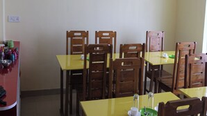 Un coin repas avec des tables jaunes et des chaises en bois, un petit réfrigérateur et une prise électrique au mur.