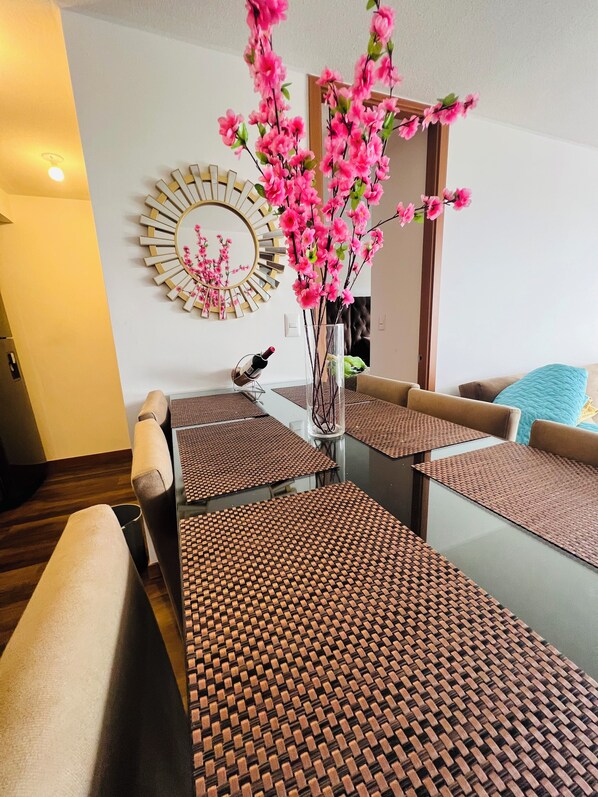 Una sala de estar moderna con un sofá, una mesa de centro y detalles decorativos, incluyendo un espejo y flores rosadas.
