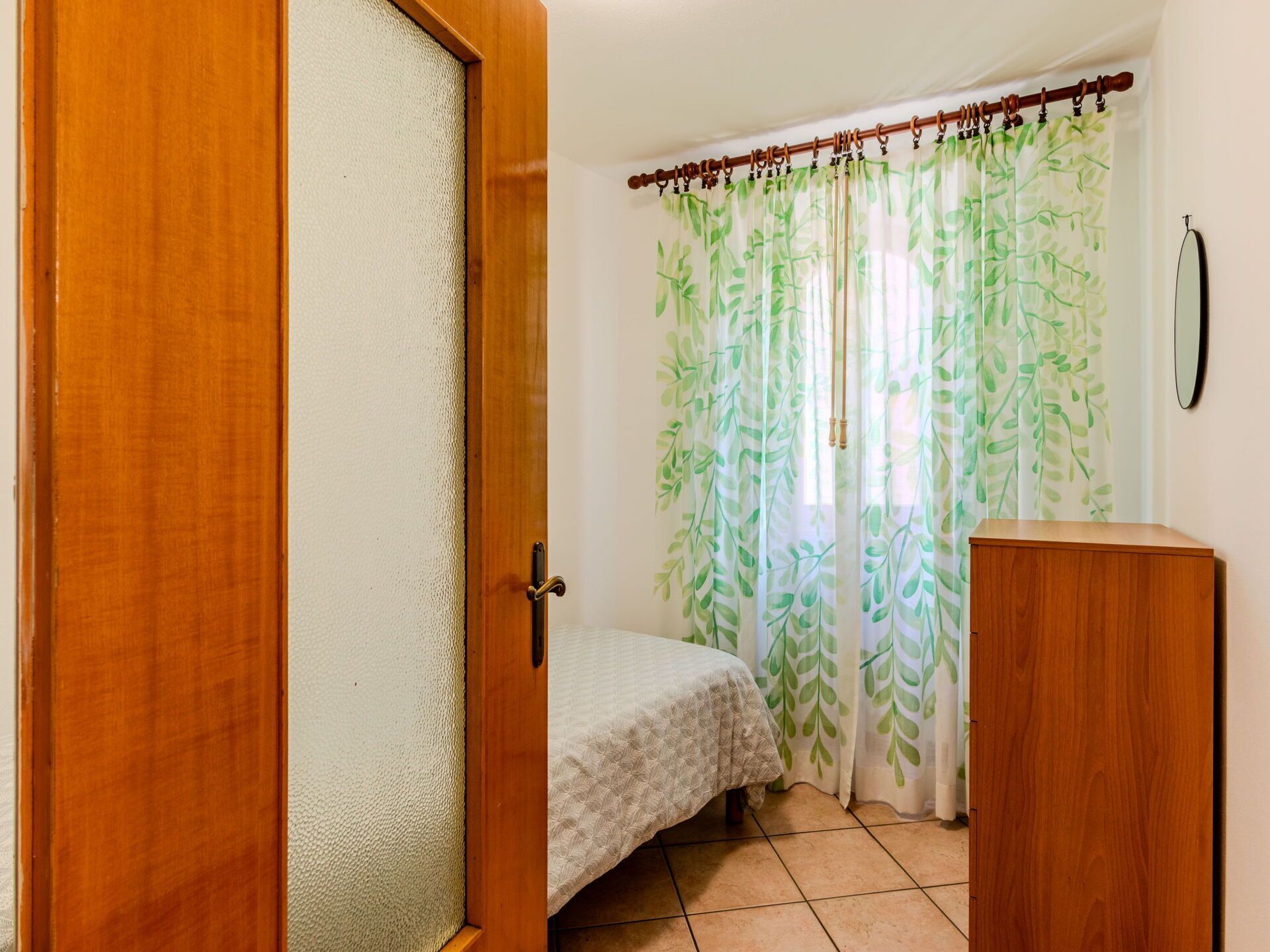 A bedroom with a bed, a wooden wardrobe, and a door leading to another room.