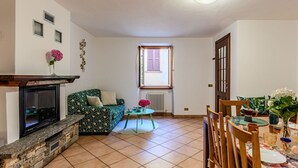 A living room with a fireplace, a sofa, a dining table set for two, and a window with shutters. - Stunning private villa for 5 people with WIFI, balcony and pets allowed (Osteno-claino)
