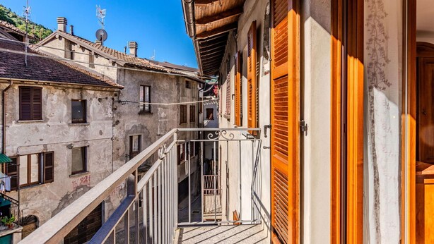 A narrow street with buildings on either side, a wooden balcony railing, and a gate leading to a courtyard. - Stunning private villa for 5 people with WIFI, balcony and pets allowed (Osteno-claino)