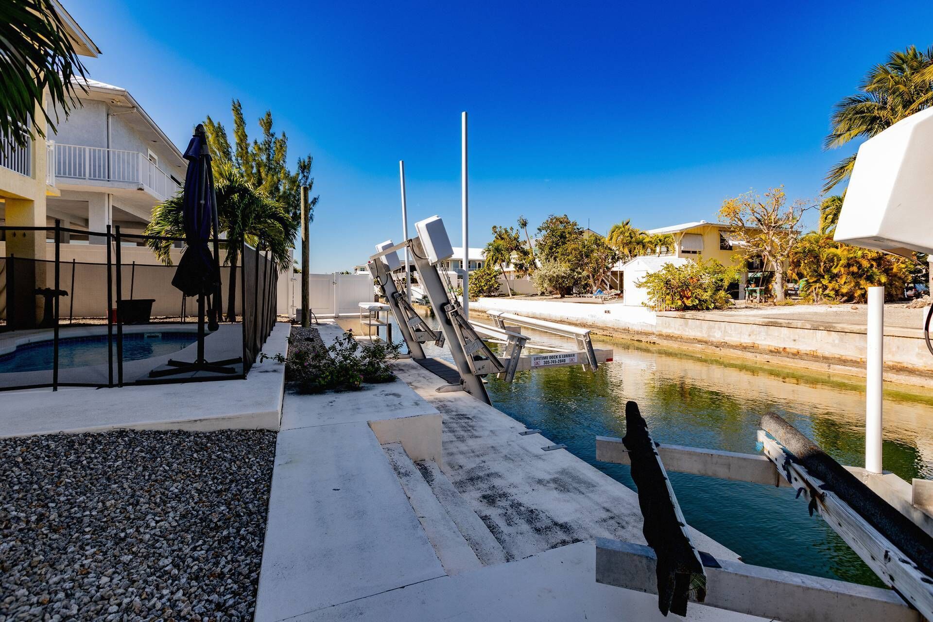 A pool area with a leaning pool ladder, a clear blue sky, and buildings in the background.