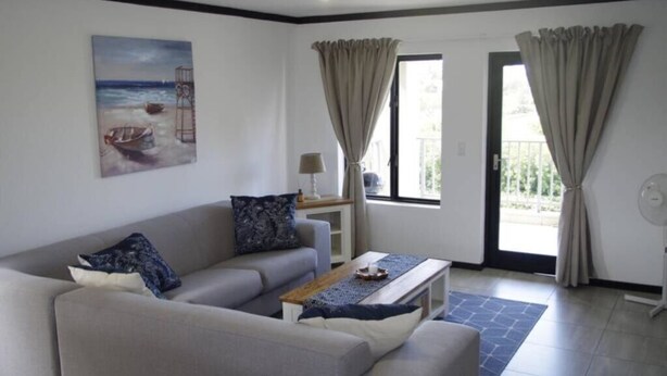Un salon avec un canapé, une table basse et un tableau représentant une scène de plage.