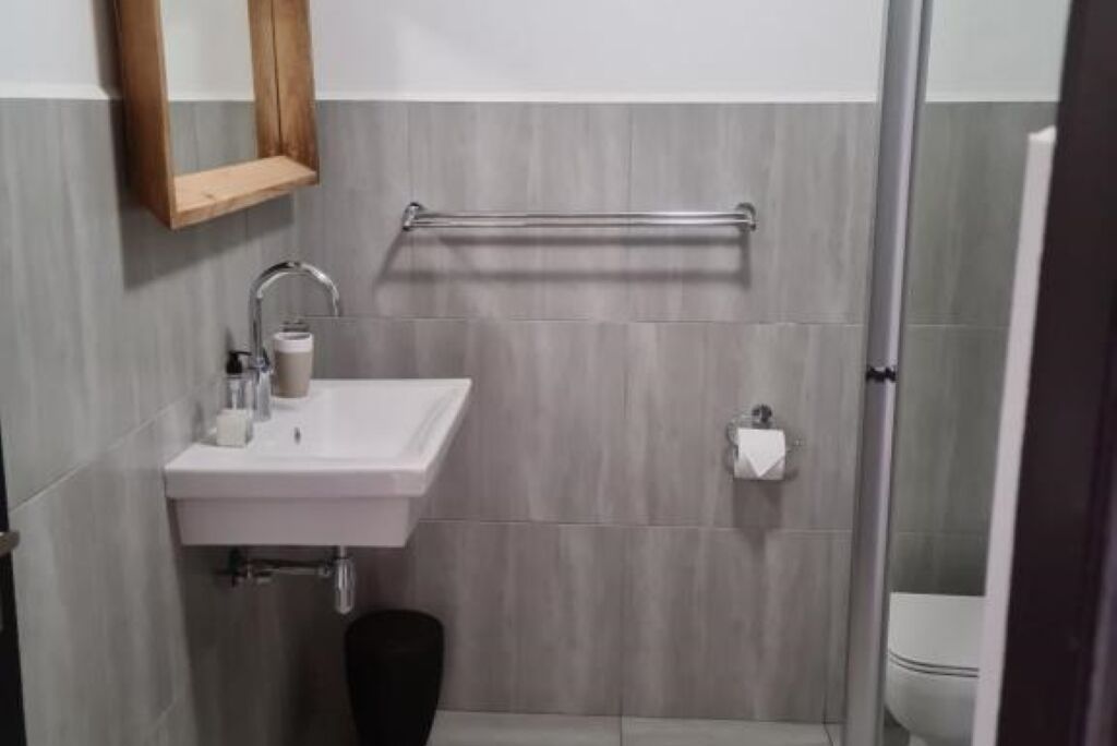 Un baño moderno con un lavamanos blanco, un espejo con marco de madera y un perchero.