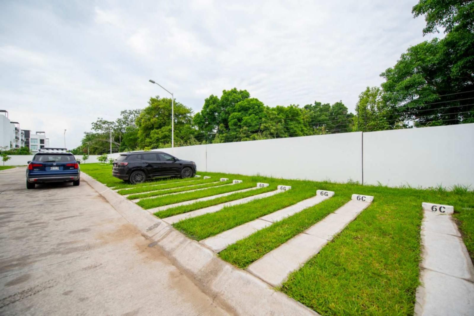 A parking area with a blue car and a black SUV, a grassy area with numbered stepping stones, and a white wall.