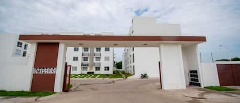 A gated entrance to a residential building complex with multiple balconies and a clear sky.