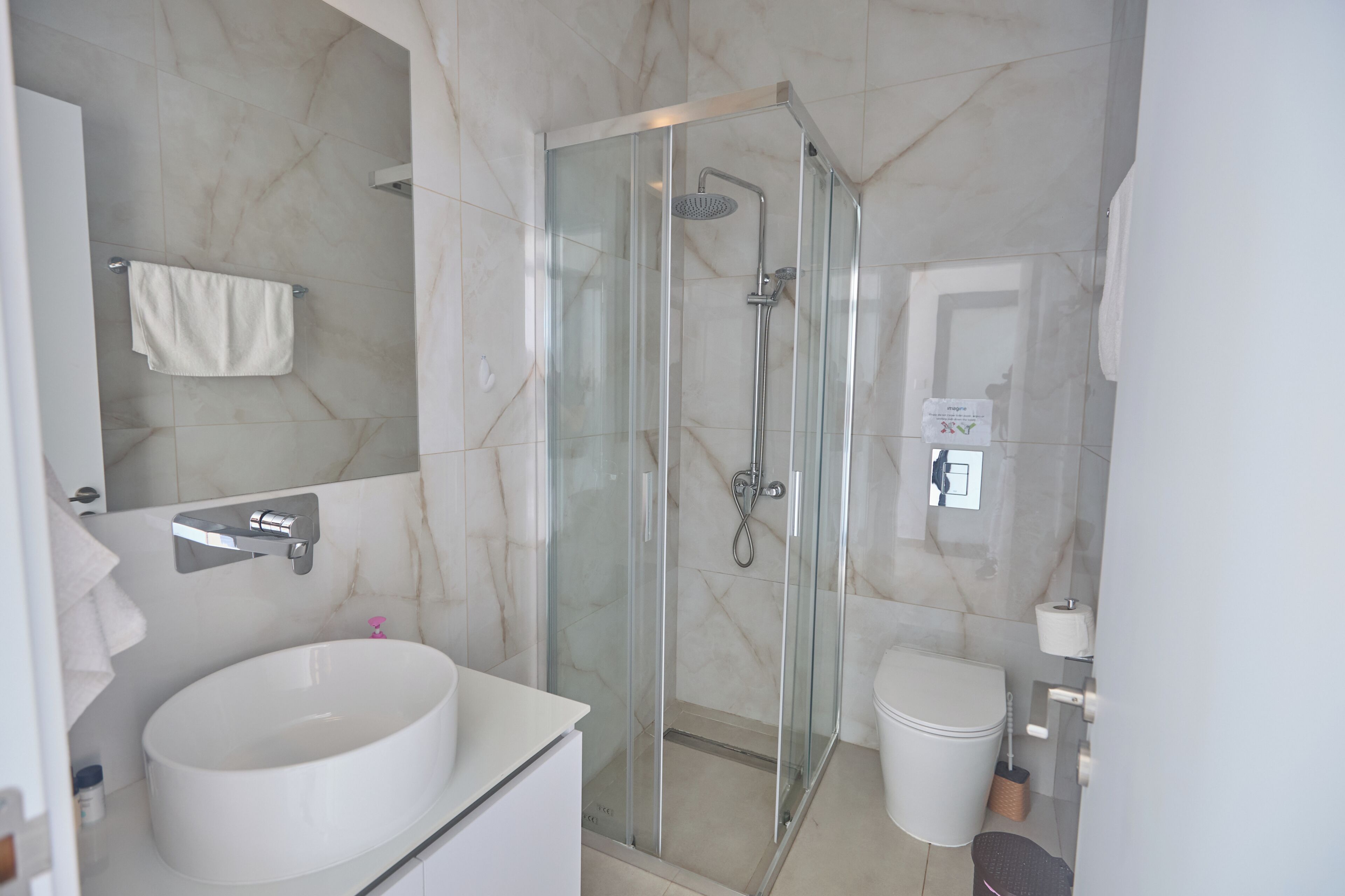 A modern bathroom with a glass-enclosed shower, a white sink, and a toilet.