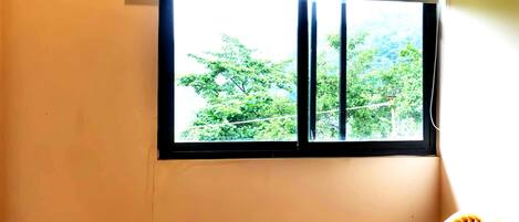 Una habitación con ventana, dos sillas de mimbre y una pequeña mesa de madera.