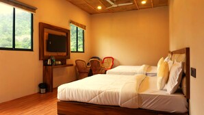A bedroom with two beds, a TV, wicker chairs, and a view of greenery outside. - ISOL Nature Resort (Rishikesh)
