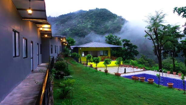 A hotel with a yellow building, a green lawn, and a mountain in the background. - ISOL Nature Resort (Rishikesh)