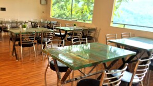 A dining area with tables and chairs, large windows with a view of greenery, and a wooden floor. - ISOL Nature Resort (Rishikesh)