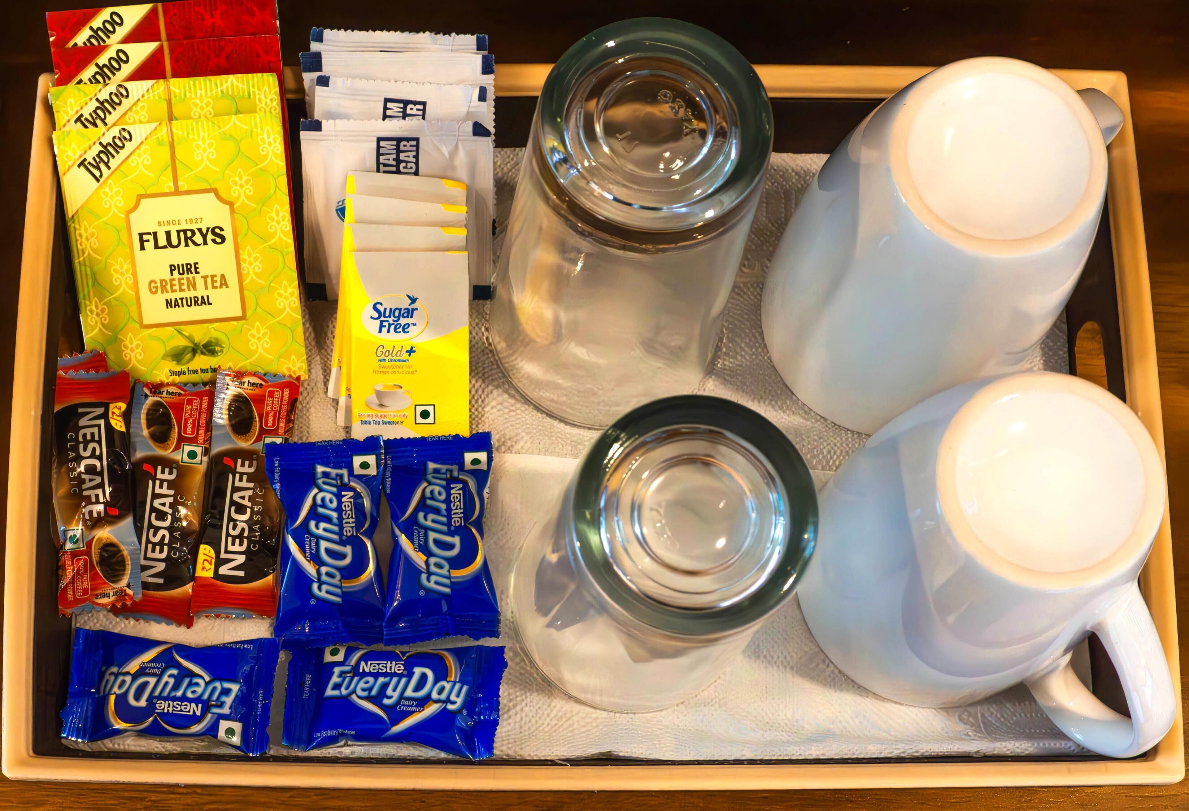 A tray with various coffee and tea products, including Nescafe and Flurys, and two white mugs.