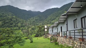A building with a stone wall and a metal railing, surrounded by lush greenery and mountains. - ISOL Nature Resort (Rishikesh)
