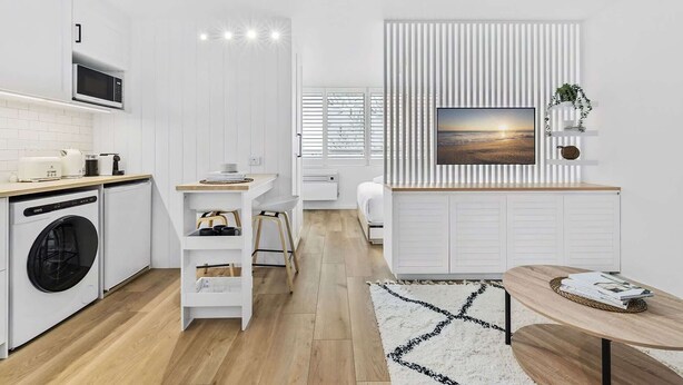 A modern kitchen with white cabinetry, a built-in microwave, and a dining area with a wooden table and chairs. - Studio3: Chic Bondi Abode with Pool & A/C (Bondi Junction)