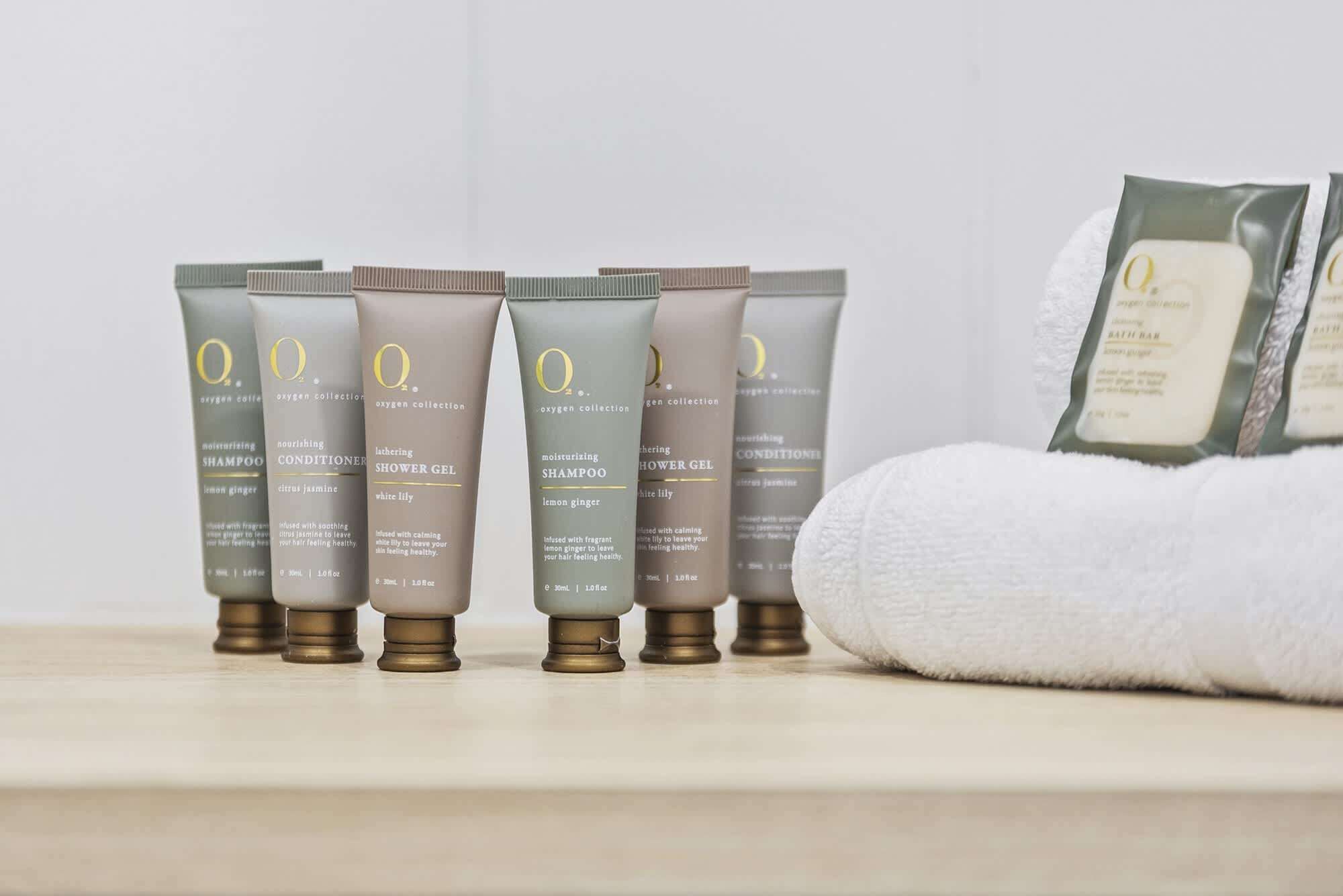 A row of toiletries on a shelf, including shampoo, conditioner, shower gel, and a bath bar.