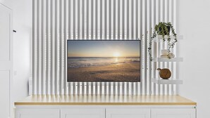 A television mounted on a white wall with vertical blinds, a wooden countertop, and a shelf with decorative items. - Studio3: Chic Bondi Abode with Pool & A/C (Bondi Junction)