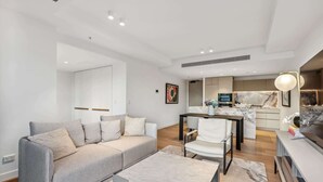 Een moderne woonkamer met een grijze bank, een klein bijzettafeltje en een eethoek met een witte stoel.