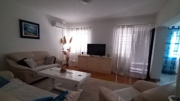 Una sala de estar con un sofá, una mesa de centro, un televisor sobre un mueble y una ventana con cortinas.