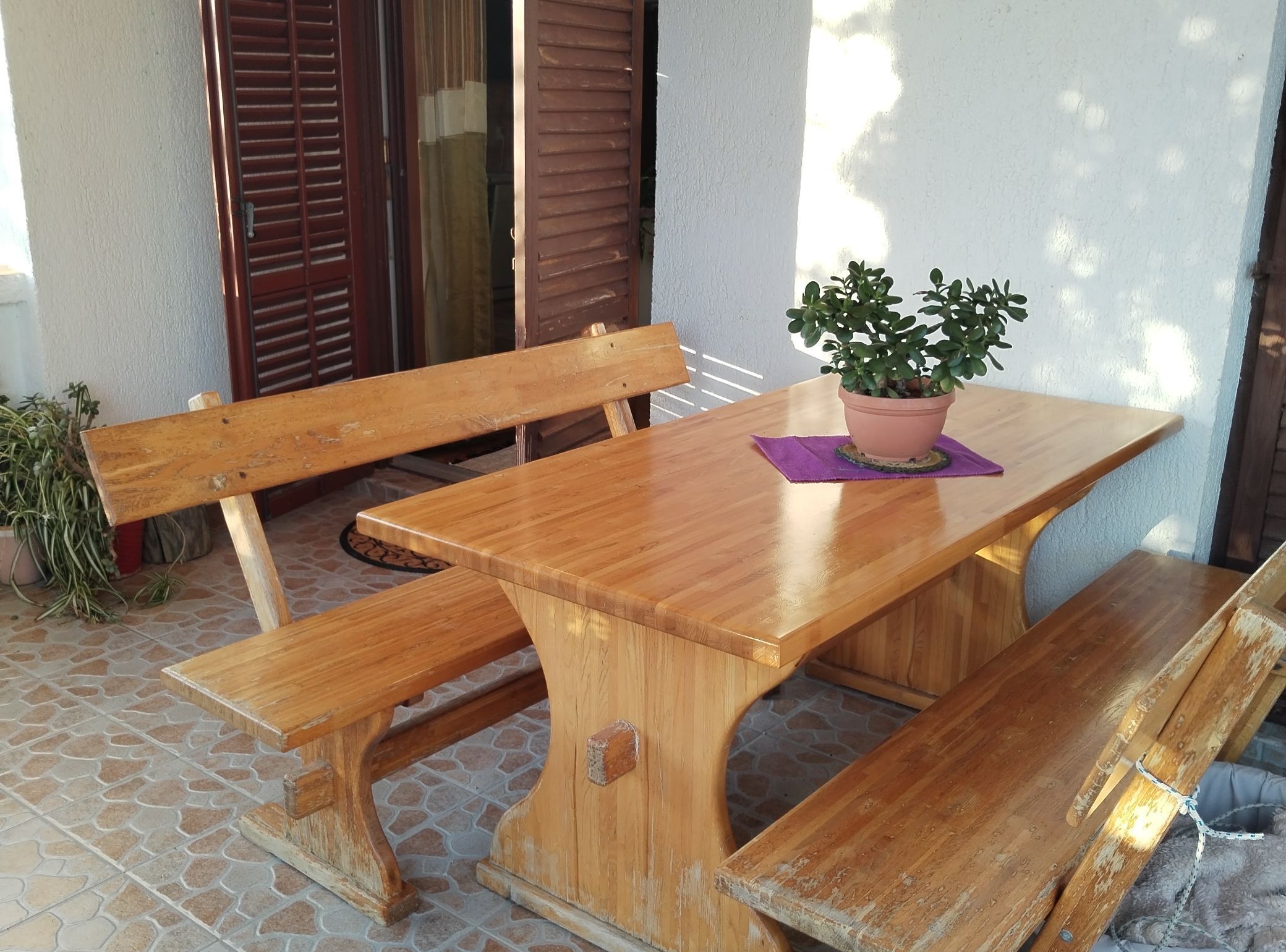 A wooden bench and table set on a tiled patio with a potted plant on the table.