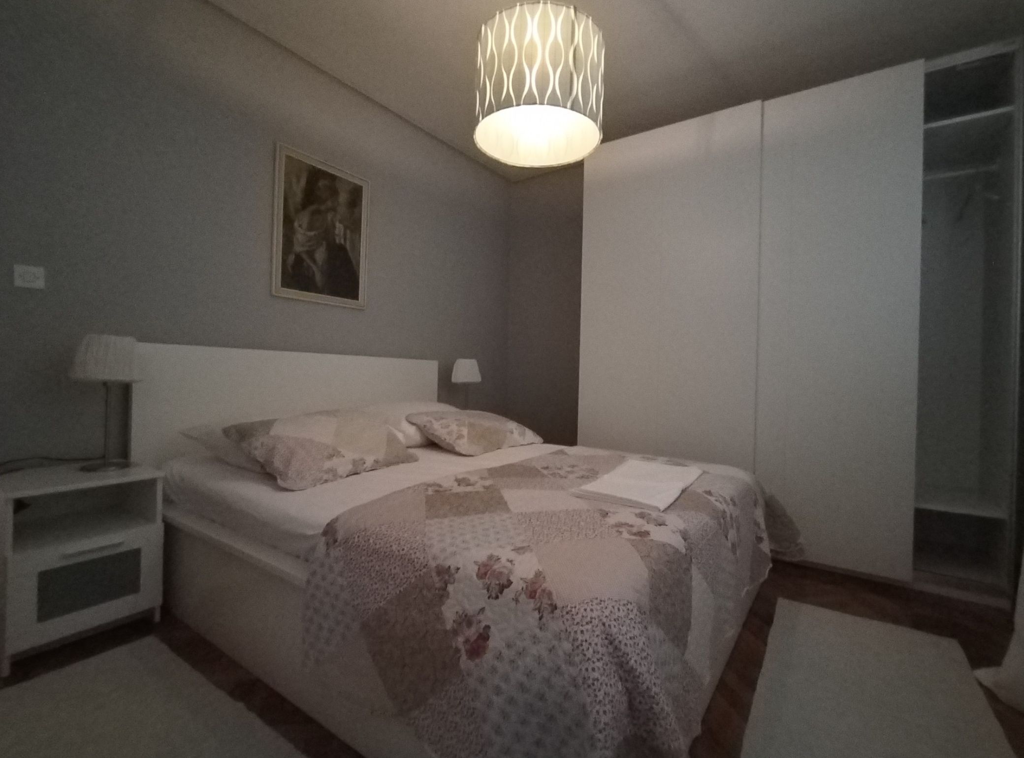 Une chambre à coucher comprenant un lit, des tables de chevet, un luminaire suspendu, une armoire et un tableau accroché au mur.