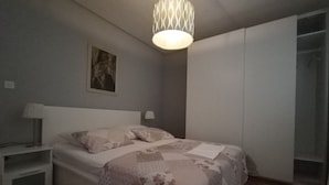 Un dormitorio con cama, mesitas de noche, lámpara colgante, armario y un cuadro en la pared.