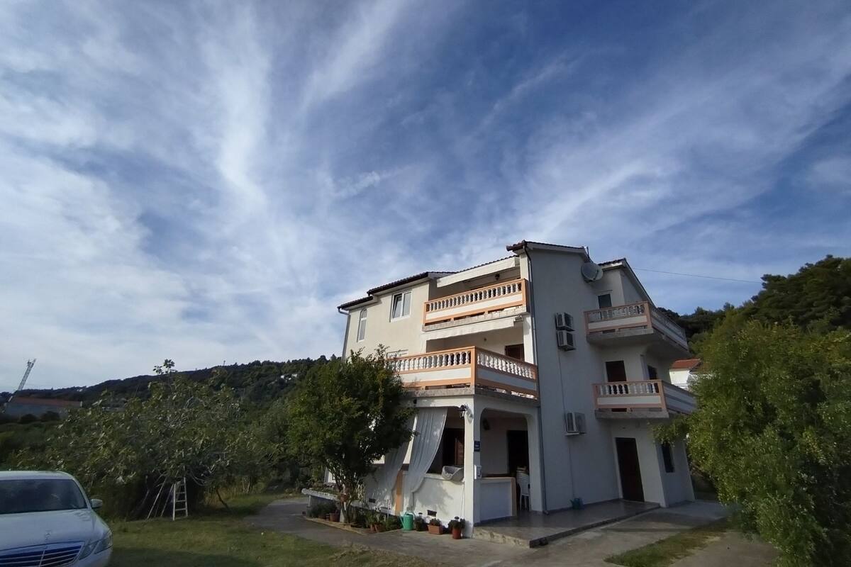 A two-story building with balconies, a driveway, and a car parked in front.