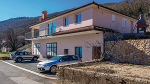 A two-story house with a balcony, a stone wall, and parked cars.