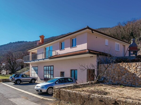 A two-story house with a balcony, a stone wall, and parked cars. - Cozy One Bedroom Apartment With Terrace (Moscenicka Draga)