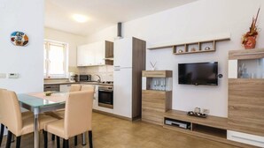 A modern kitchen with white cabinets, a dining table with chairs, and a TV mounted on the wall.