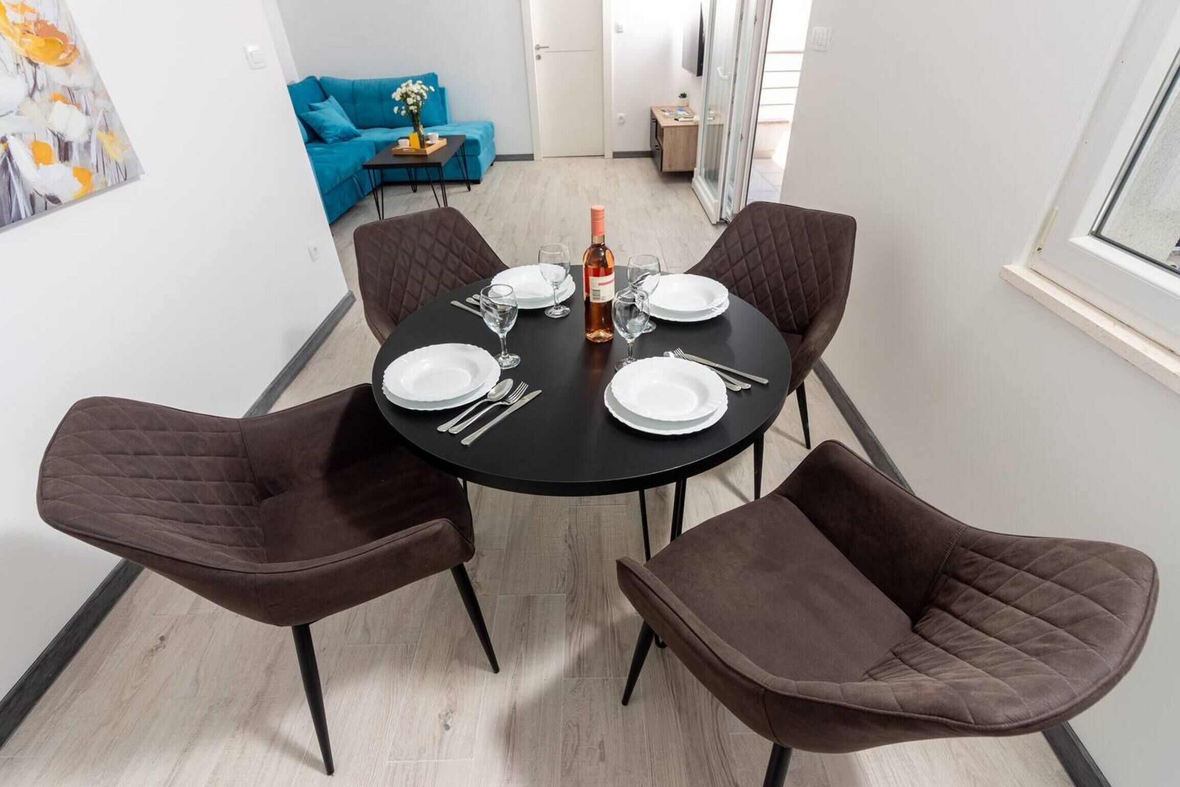 Comedor con una mesa redonda dispuesta para cuatro personas, con platos, cubiertos y una botella de vino.