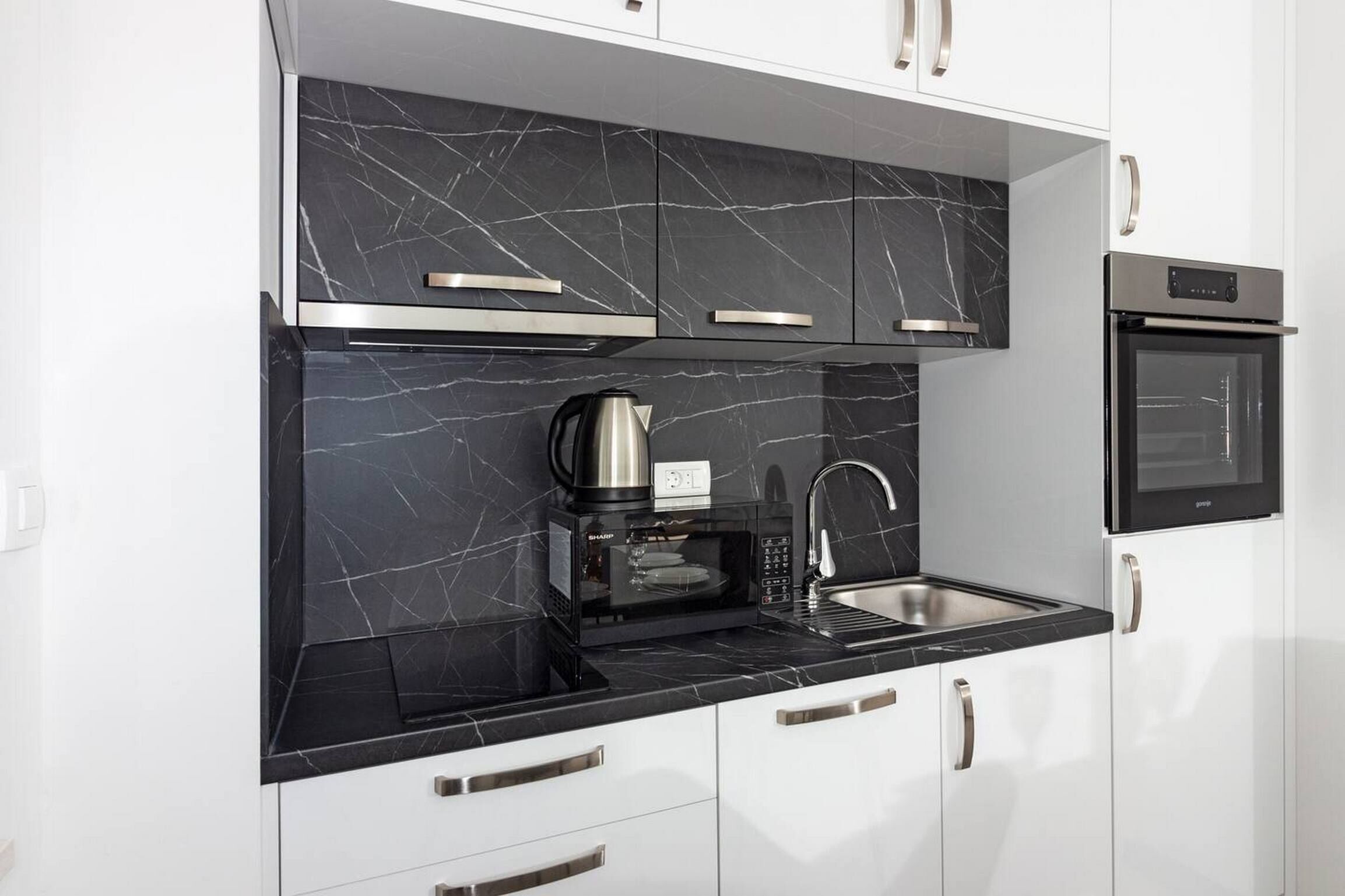 Una cucina moderna con piani di lavoro in marmo nero, elettrodomestici in acciaio inossidabile e mobili bianchi.